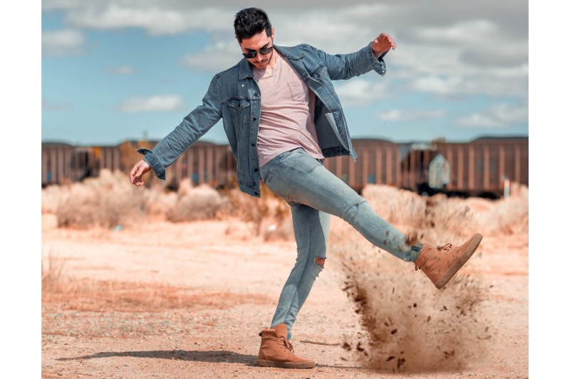 Barbat in denim si cizme de desert care ridica nisipul.