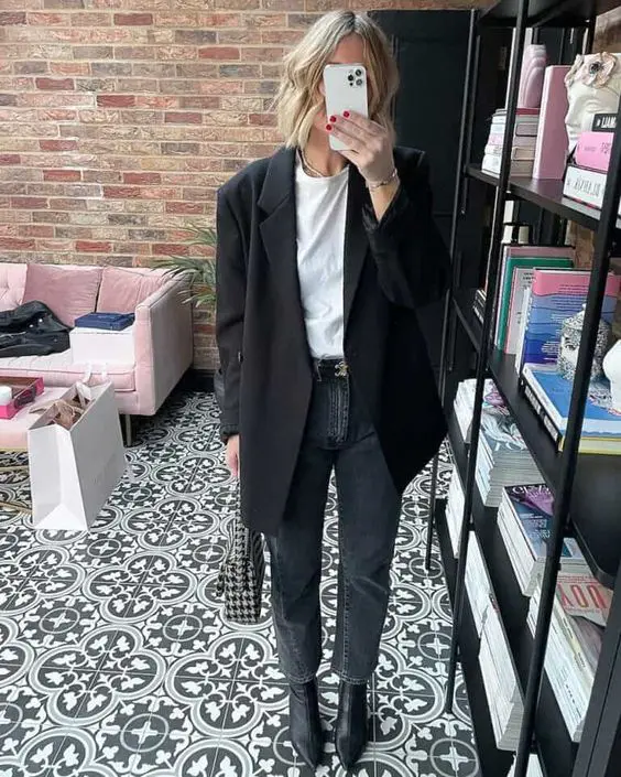 un tricou alb, blugi taiati gri, cizme negre cu varf ascutit, un blazer negru supradimensionat si o geanta imprimata pentru un aspect monocromatic cool